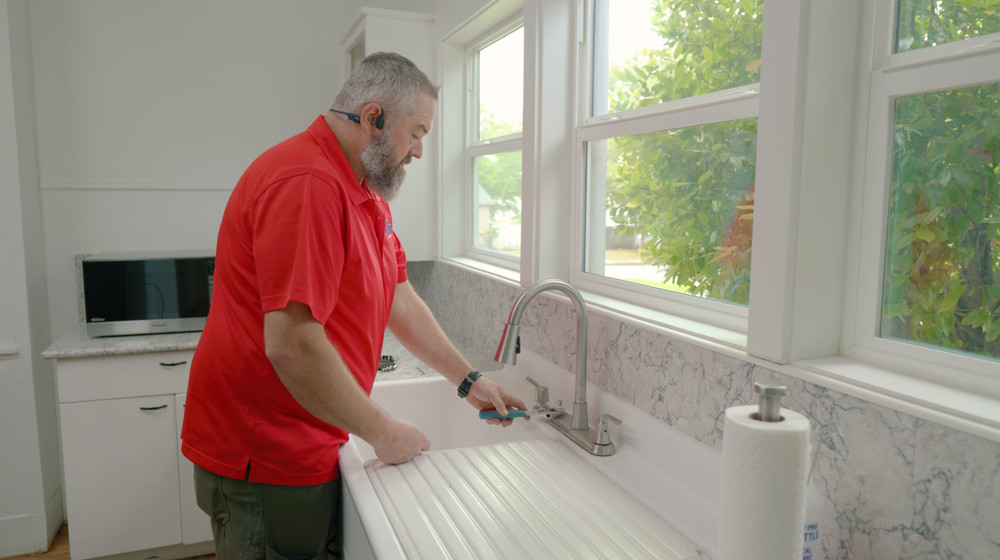 A We The Plumbers plumber checking a kitchen faucet at a farmhouse sink