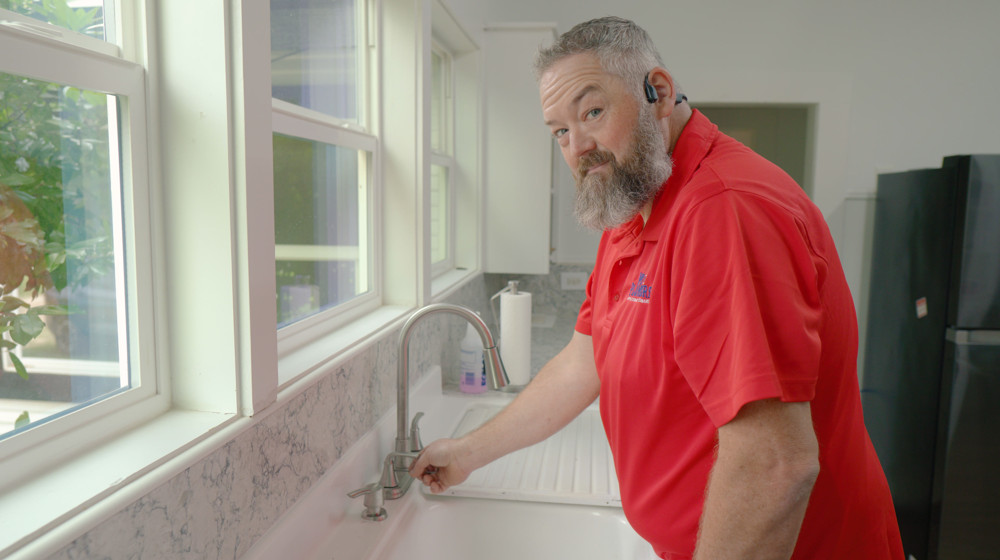 A plumber checking a kitchen faucet's water flow