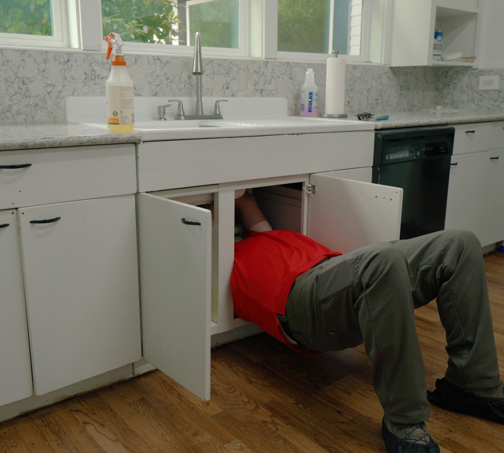 A plumber working inside the cabinet under a kitchen sink