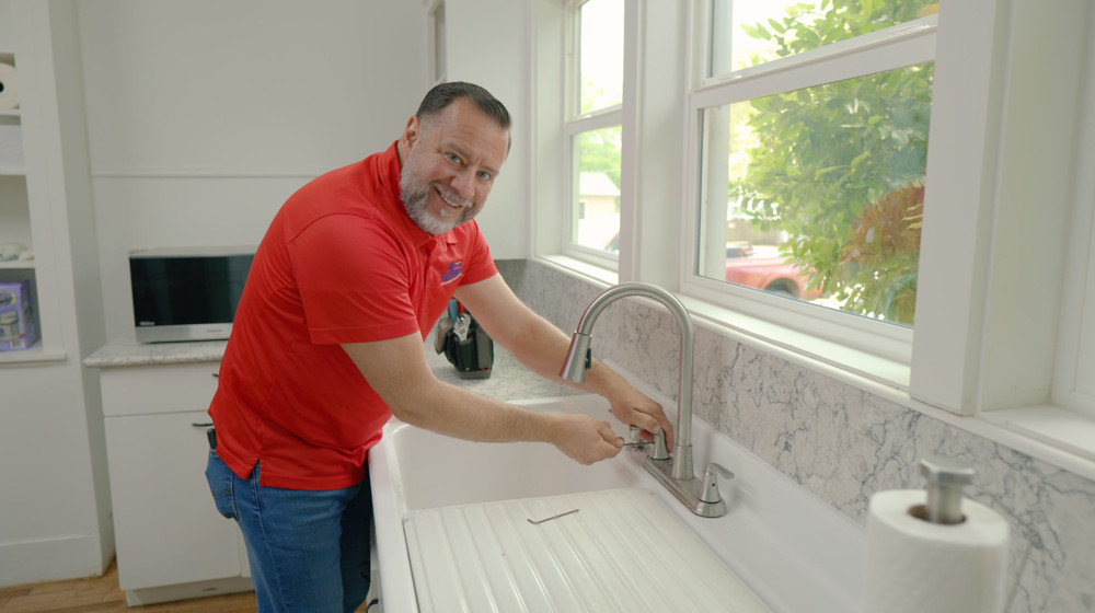 A plumber smiling while working on a kitchen faucet