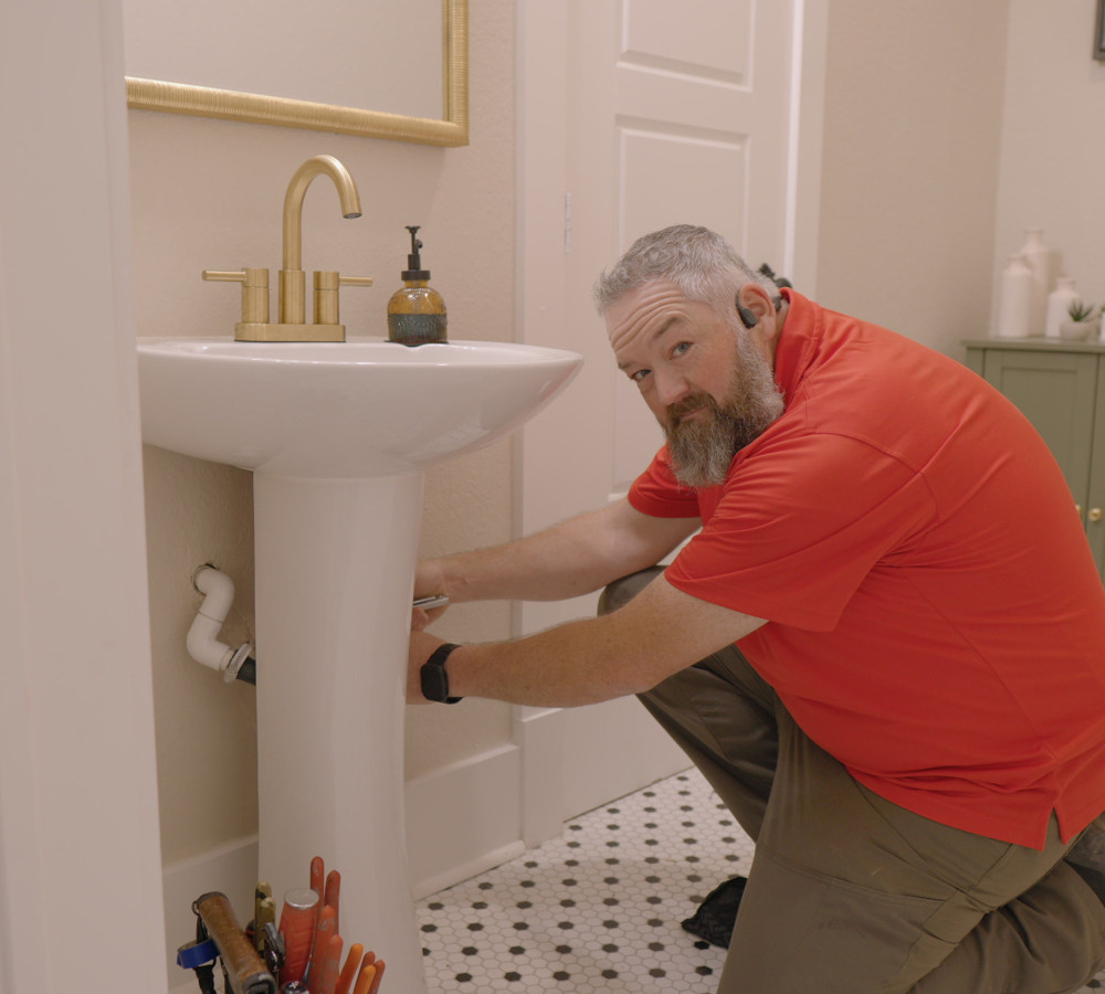 A plumber working on the drain under a bathroom pedestal sink