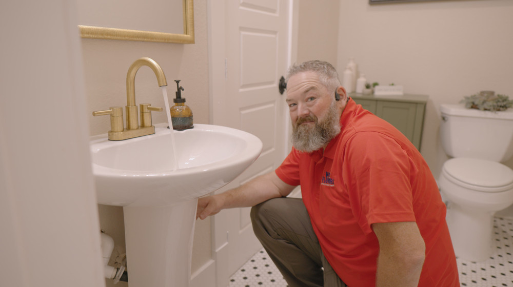 A plumber reaching under a bathroom pedestal sink