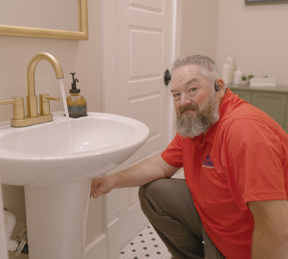 A plumber reaching under a bathroom pedestal sink