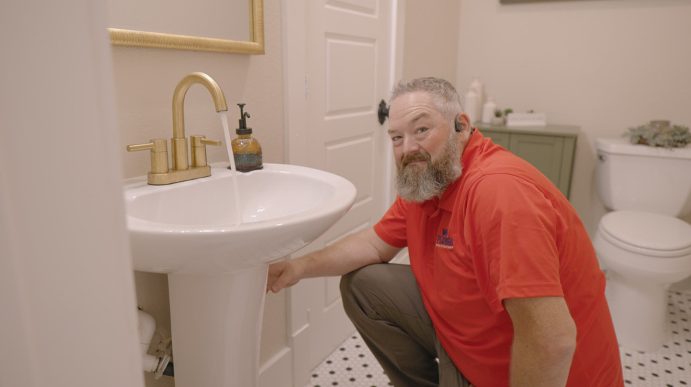 A plumber working beside a bathroom sink and toilet