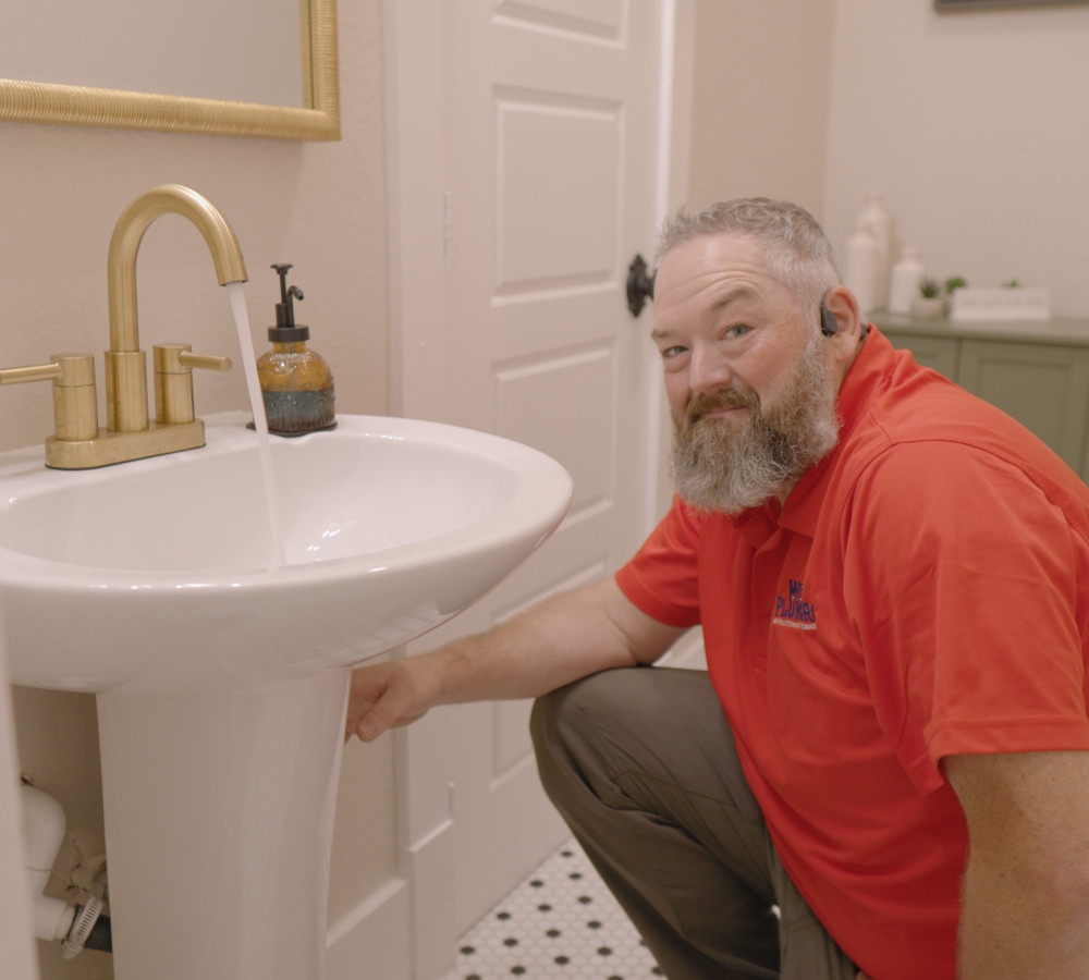 A plumber working beside a bathroom sink and toilet