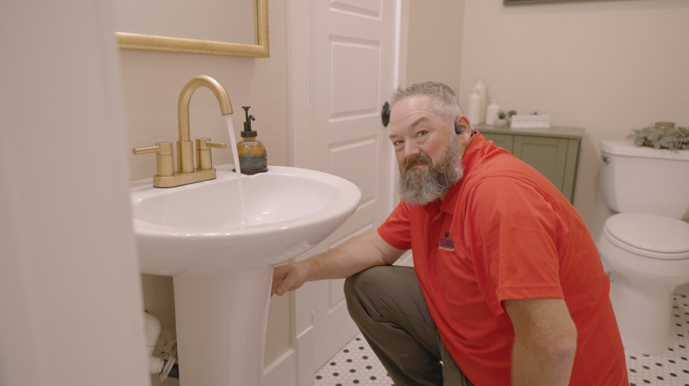 A plumber checking the plumbing under a bathroom sink