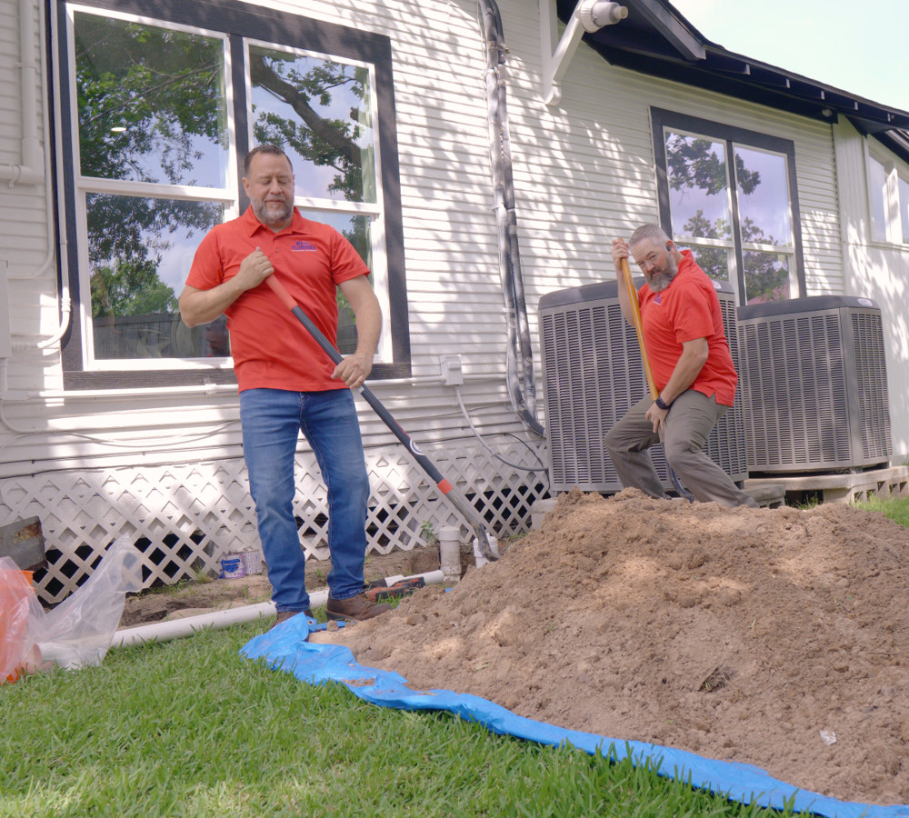 Plumbers digging to reach a sewer line beside a house