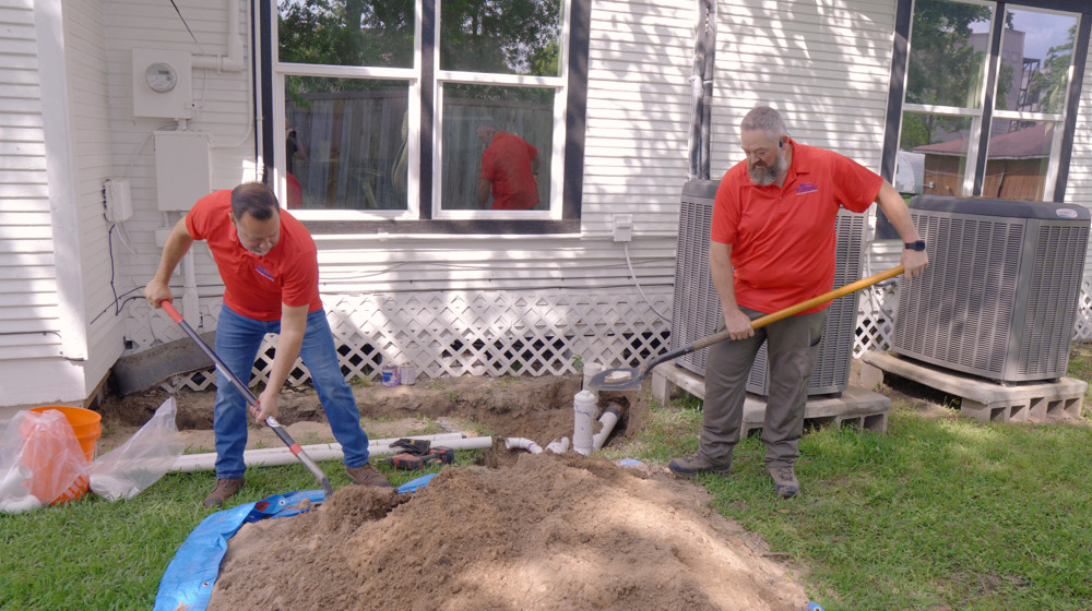 A plumber digging out a sewer line next to a house
