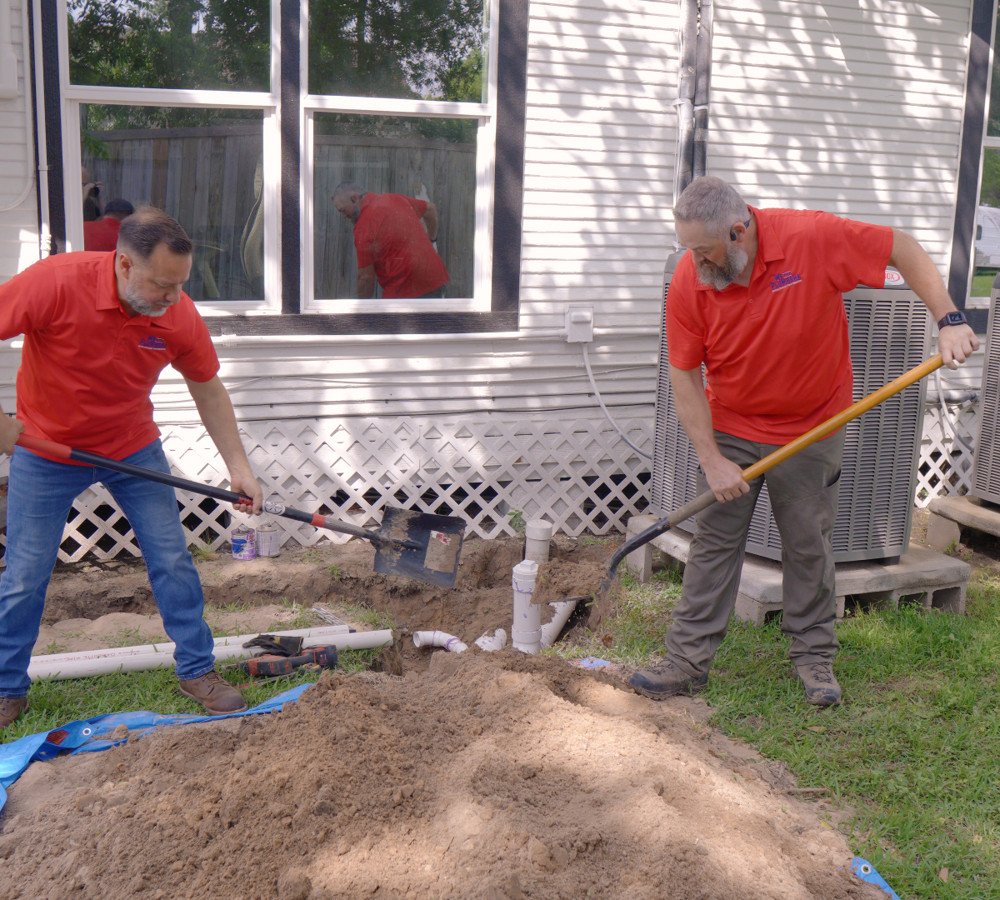 Two plumbers working a shovel and pick at a sewer dig