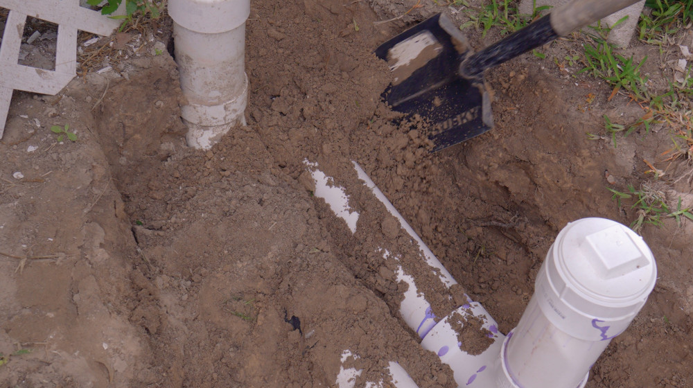 An exposed white sewer pipe in an open trench