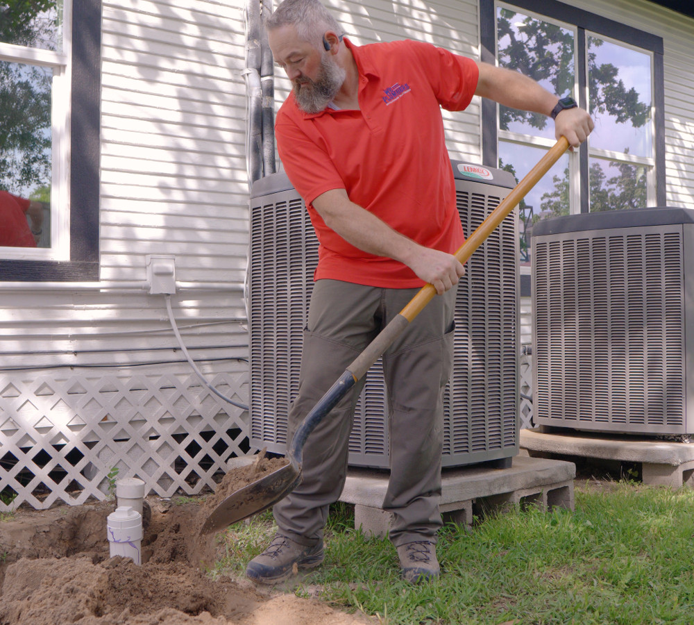 A plumber digging beside an air conditioning unit