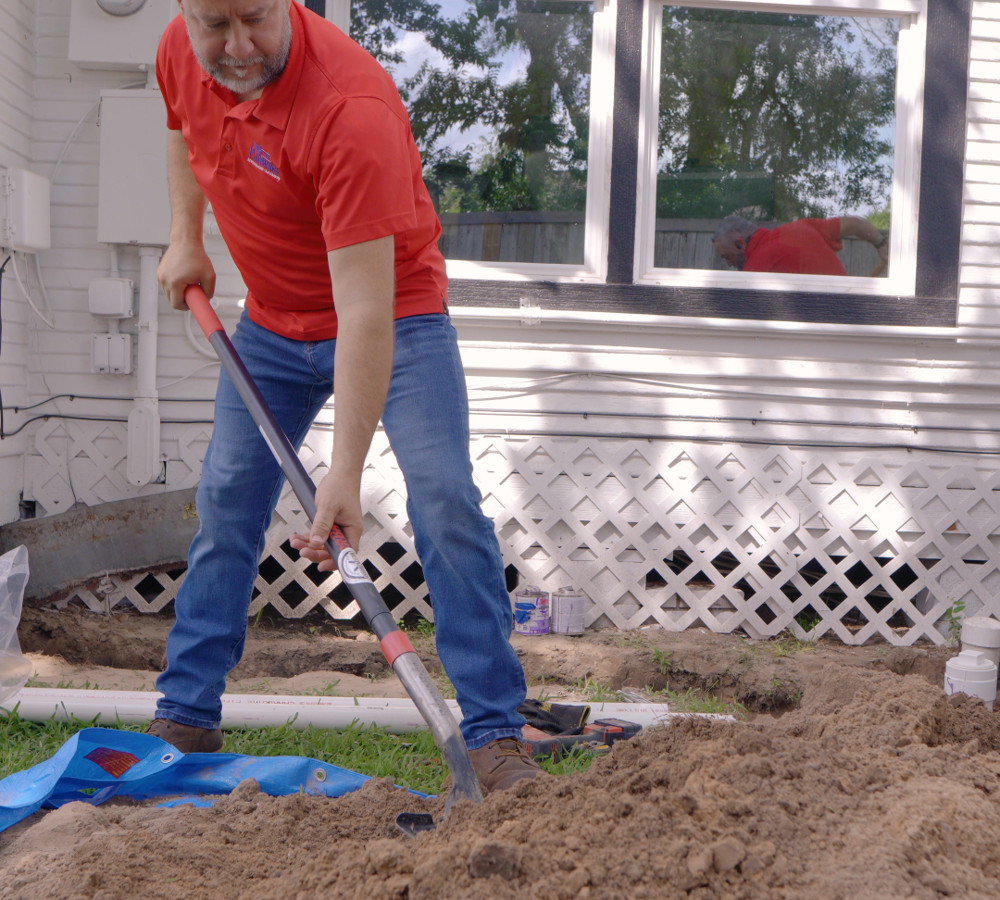 A plumber working a shovel at the edge of a trench