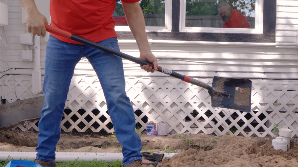 A plumber digging along the side of a house