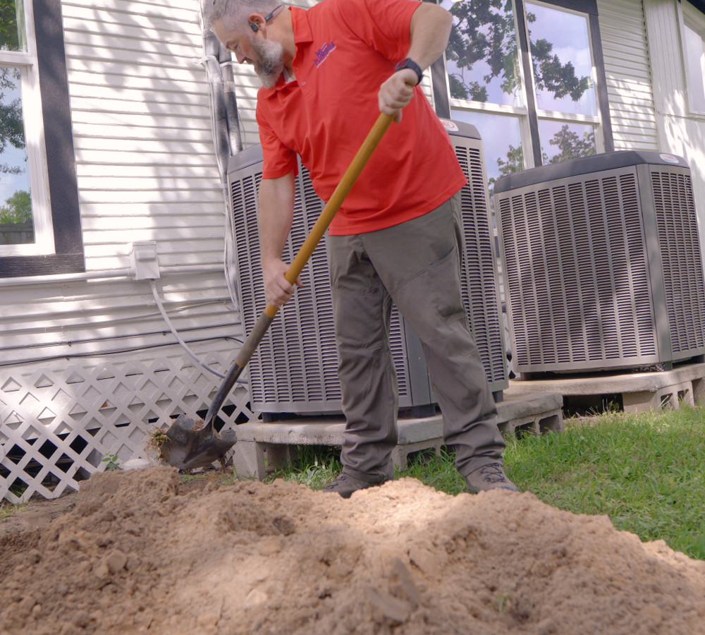 A plumber digging near a house's foundation