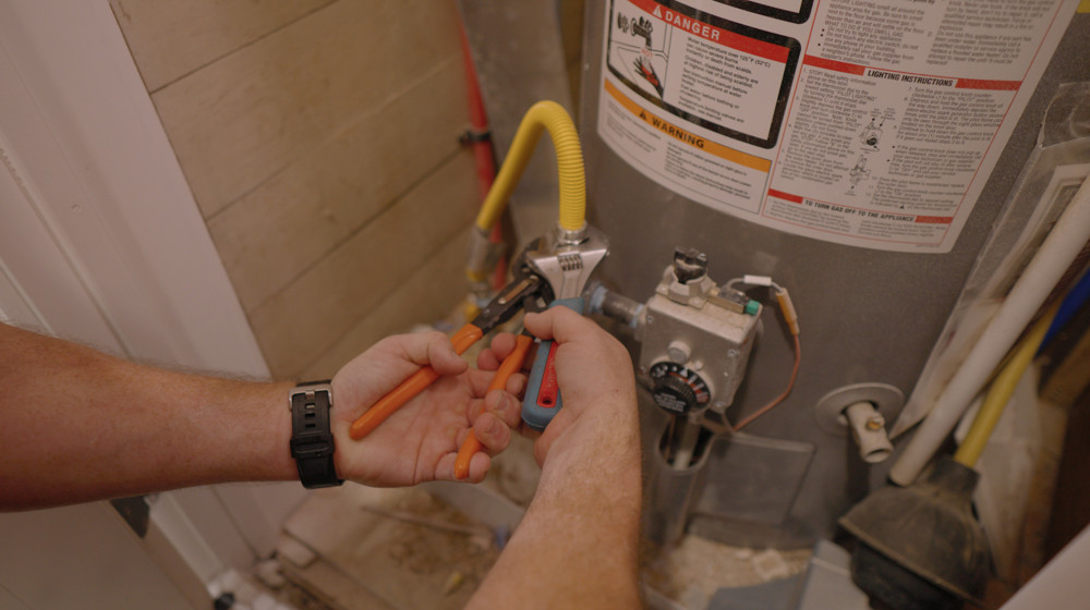 A plumber's hands working on a water heater's gas valve and connections