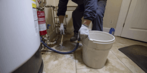 Photo of a Texas homeowner flushing a water heater using a hose and basic tools in a utility room, illustrating essential maintenance to extend appliance lifespan.